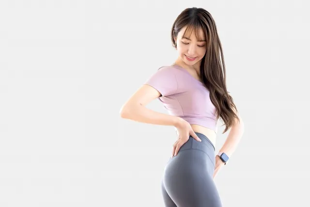ピラティスの紫色のウェアを着た女性が自身のくびれた腰を見て微笑んでいる