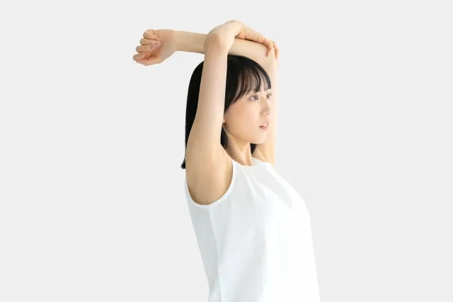 ピラティスのストレッチで片手を肩の上に上げもう一方の手で肘を掴んでいる女性