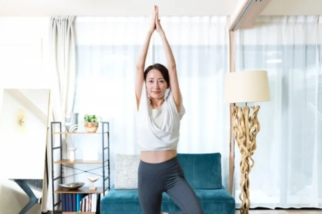 自宅の部屋でヨガの木のポーズをしている白いウェアの女性