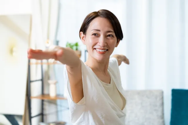 自宅でヨガの戦士のポーズⅡをしている白いウェアの女性
