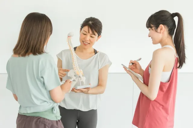 ピラティスで骨格の勉強を教えている女性と習っている女性2人