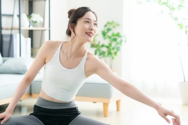 自宅の部屋でピラティスのストレッチをしている白いウェアの女性