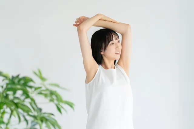 自宅で両手を上げてストレッチをしている白いウェアの若い女性