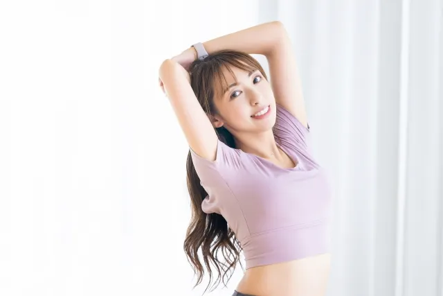自宅で両手を上げてストレッチしている紫色のウェアの女性