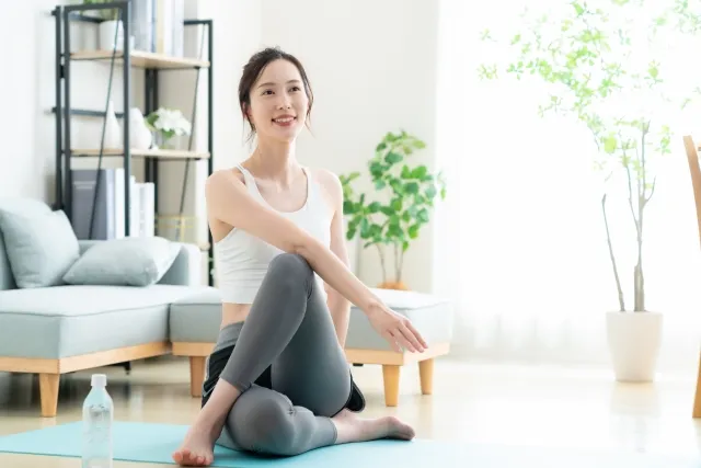自宅でヨガマットの上でストレッチをしている白いウェアの女性