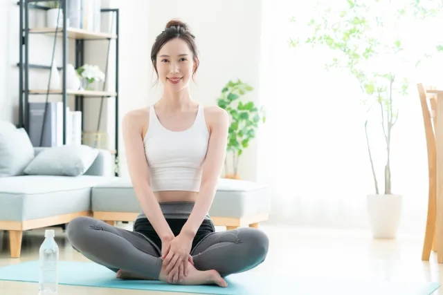 自宅でヨガマットの上であぐらをしている白いウェアの女性