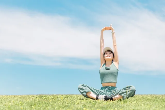 天気のいい空の下で両手を組んで上に伸ばすストレッチをする女性