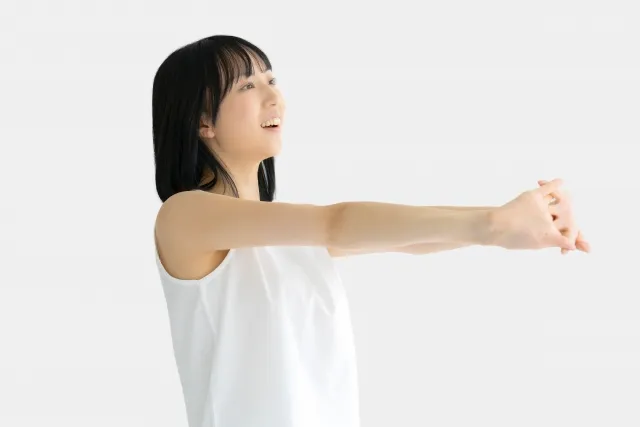 自宅で両手を組んで前方にストレッチをしている白いウェアの女性