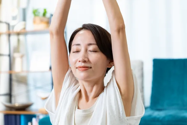 自宅の部屋で両手を頭上に上げてストレッチをしている女性の顔のアップ