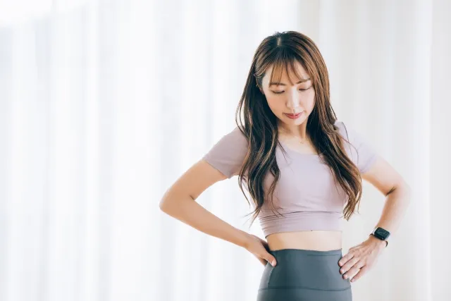 自宅でウエイトに両手を当てて気にしている紫色のウェアの女性