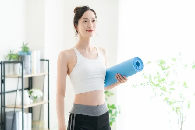 自宅で巻いたマットを持っている白いウェアの女性