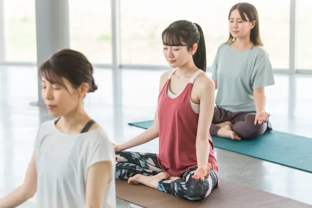ピラティススタジオでマットの上でポーズを取りながら瞑想をしている女性3人