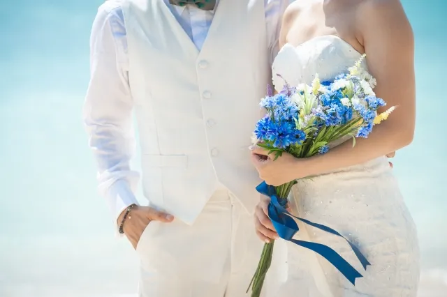 リゾート結婚式で屋外でブーケを持つ花嫁の背中に手を添えて寄り添う花婿