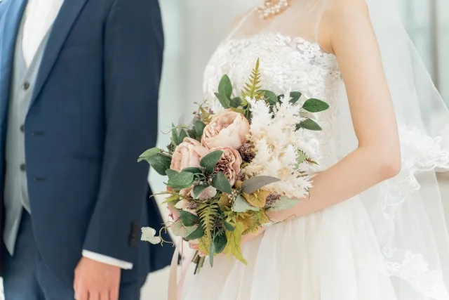 結婚式でブーケを持つ白いウエディングドレスの花嫁と紺色のスーツを着る花婿