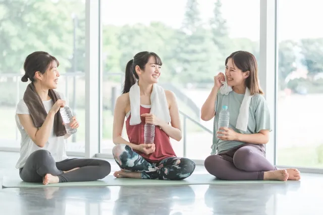 スタジオでのトレーニングの後にタオルを首にかけて水を飲みながら談笑している女性3人