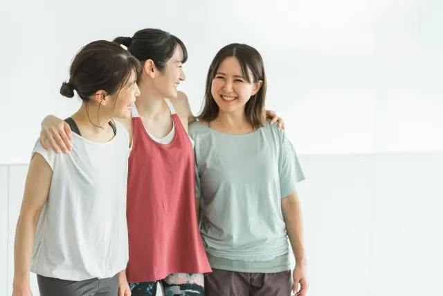 ピラティスウェア着て肩を組みながら談笑している女性3人