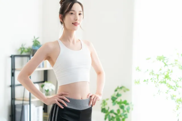自宅で腰に両手を添えて背筋を伸ばしている白いウェアの女性