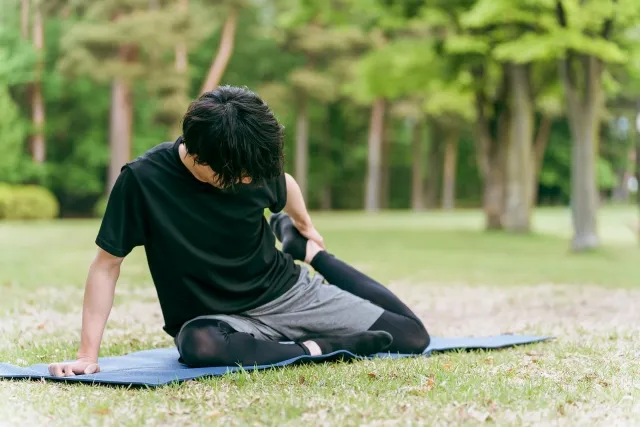 公園でヨガマットの上で鳩のポーズをするために足を上げようとして上がらない黒いウェアを着た男性