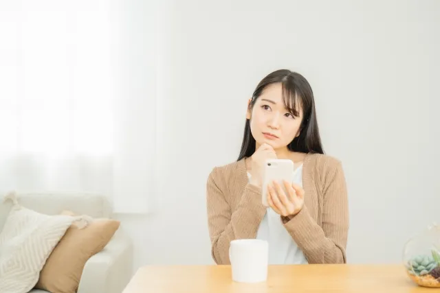 左手でスマホを持ち右手を顎に当てて悩んでいる女性
