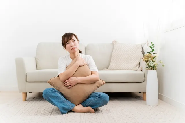 ソファの前でクッションを抱いて座り悩んでいる女性