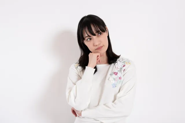 右手を顎に当てて左手で右手の肘を支えながら悩んでいる女性