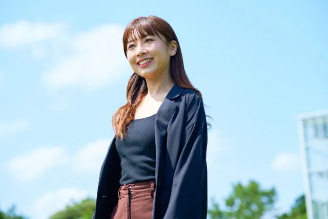 青空の下でジャケットを着た女性が笑顔で歩いている様子