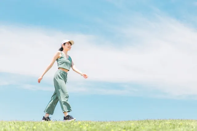 青空の下でトレーニングウェアを着た女性が笑顔で歩いている様子