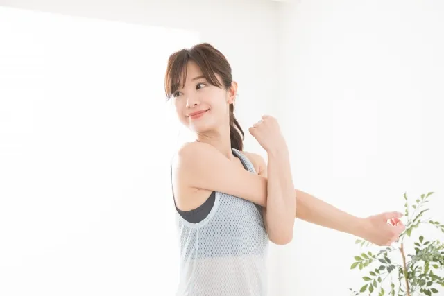 伸ばした右手を左手で抑えてストレッチしている女性