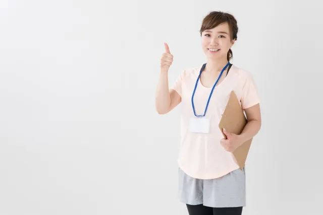 左手でバインダーを小脇に抱えて、右手の親指を上げていいねするインストラクターの女性