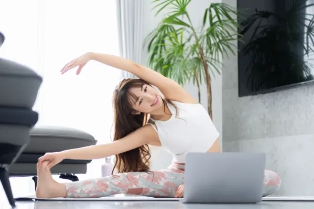 ノートパソコンを見ながらオンラインで体をひねったポーズをしている女性
