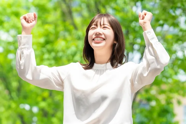 木々をバックに両手を上げガッツポーズする女性