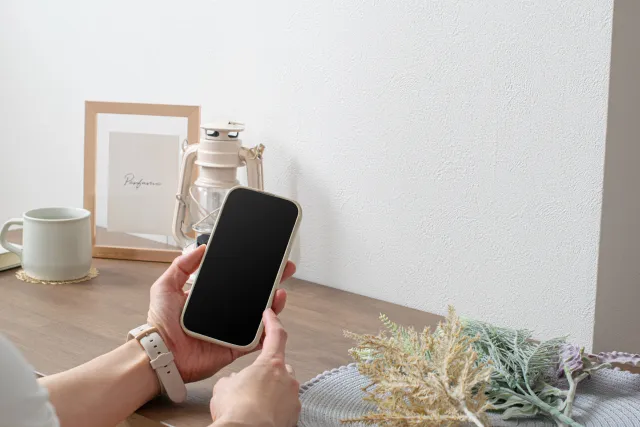 テーブルの上でスマホを操作する左手に時計をしている女性の手