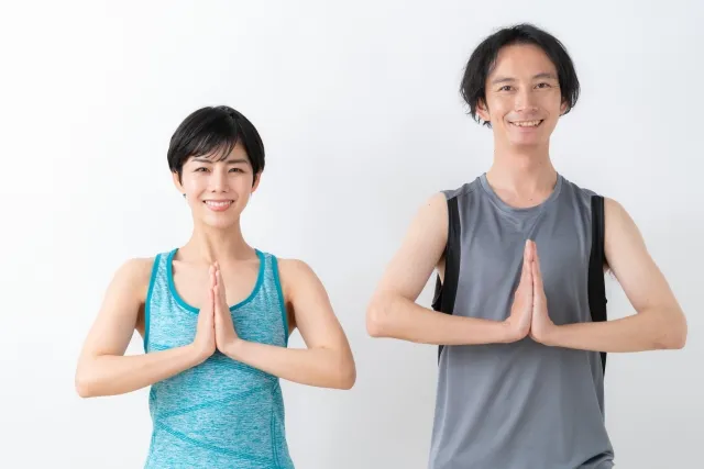 両手を合わせて体の前で合掌をしている笑顔の女性と男性