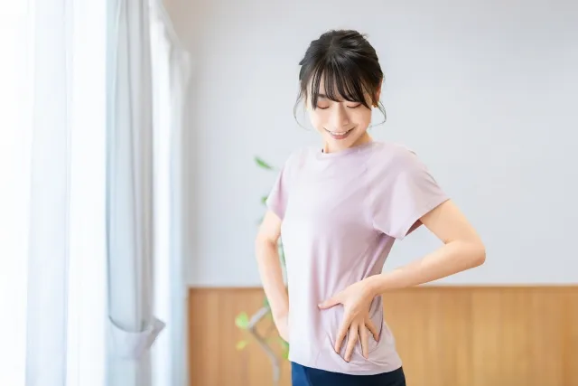 室内で左手を脇腹に当ててボディチェックをする紫色のウェアの女性
