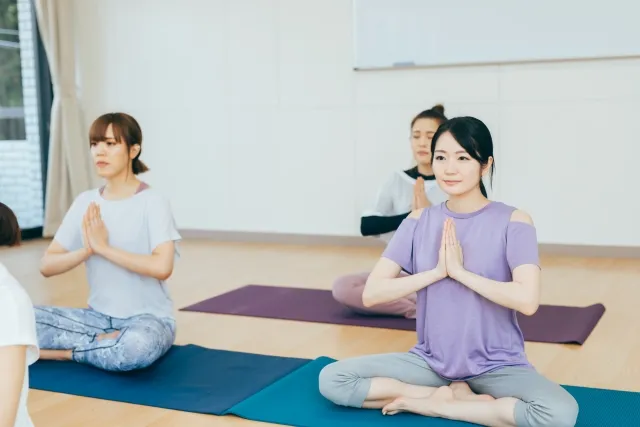 スタジオでヨガマットの上で胡坐をして両掌を合わせている女性たち
