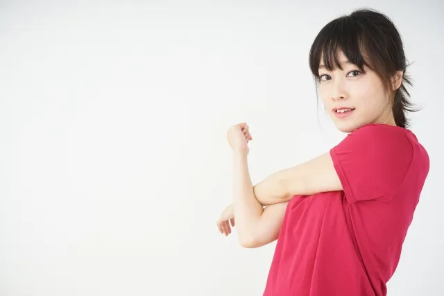 左腕を右腕で抱えてストレッチをする赤色のウェアを着た女性