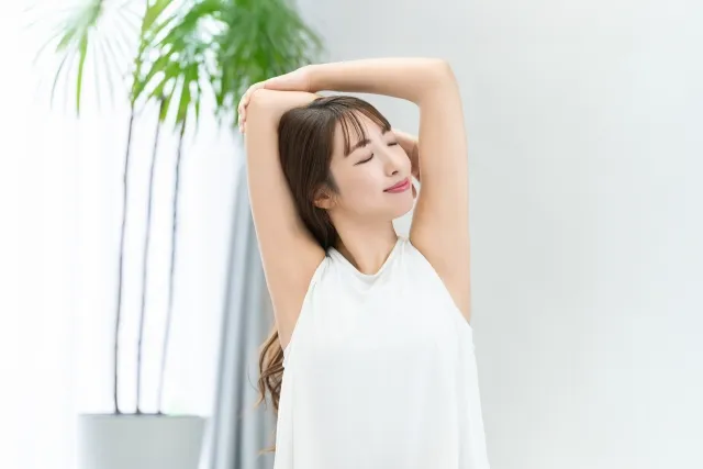 白いウェアを着た女性が両腕を頭の後ろで組んでいる様子