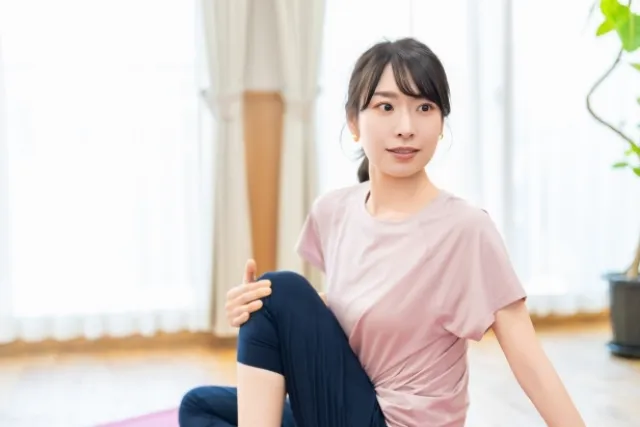 ヨガマットの上で片膝を立てて腰をひねってストレッチする紫色のウェアの女性