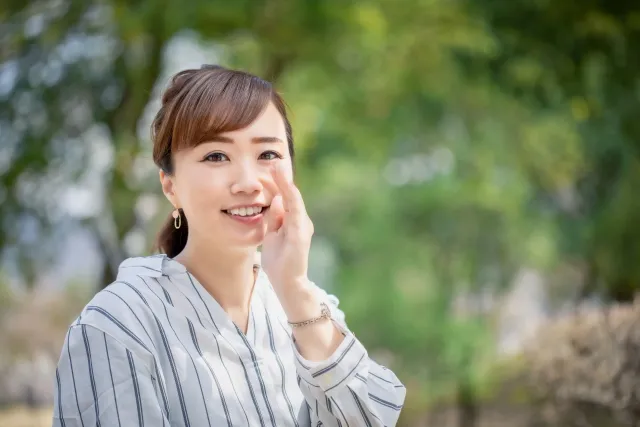 公園で口元に手を置き何かをささやいている女性