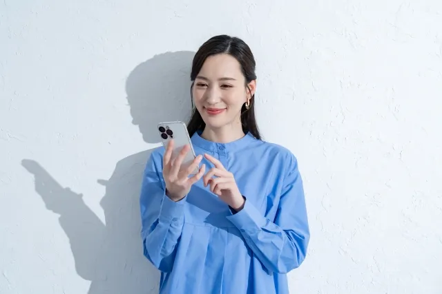 笑顔でスマホを操作している青い服を着た女性