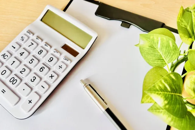 バインダーに挟まれた紙の上に白い電卓とボールペンが置かれている