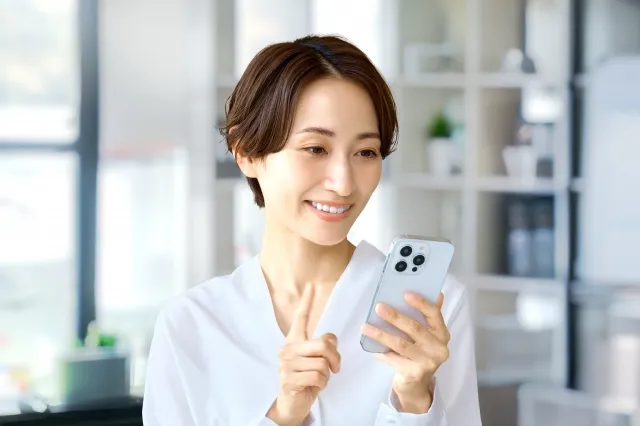 自宅にて左手で白いスマホを持って右手の人差し指で操作しようとしている女性