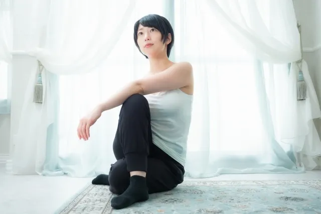 自宅のカーペットの上で右ひざを立てて体をねじってストレッチする髪の短い女性